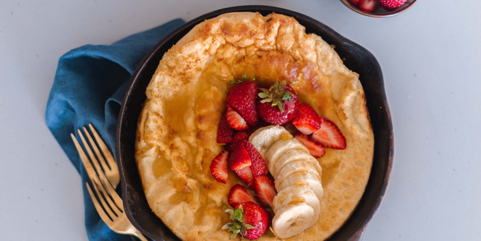 Puffed pancake in a cast iron skillet served with berries and banana