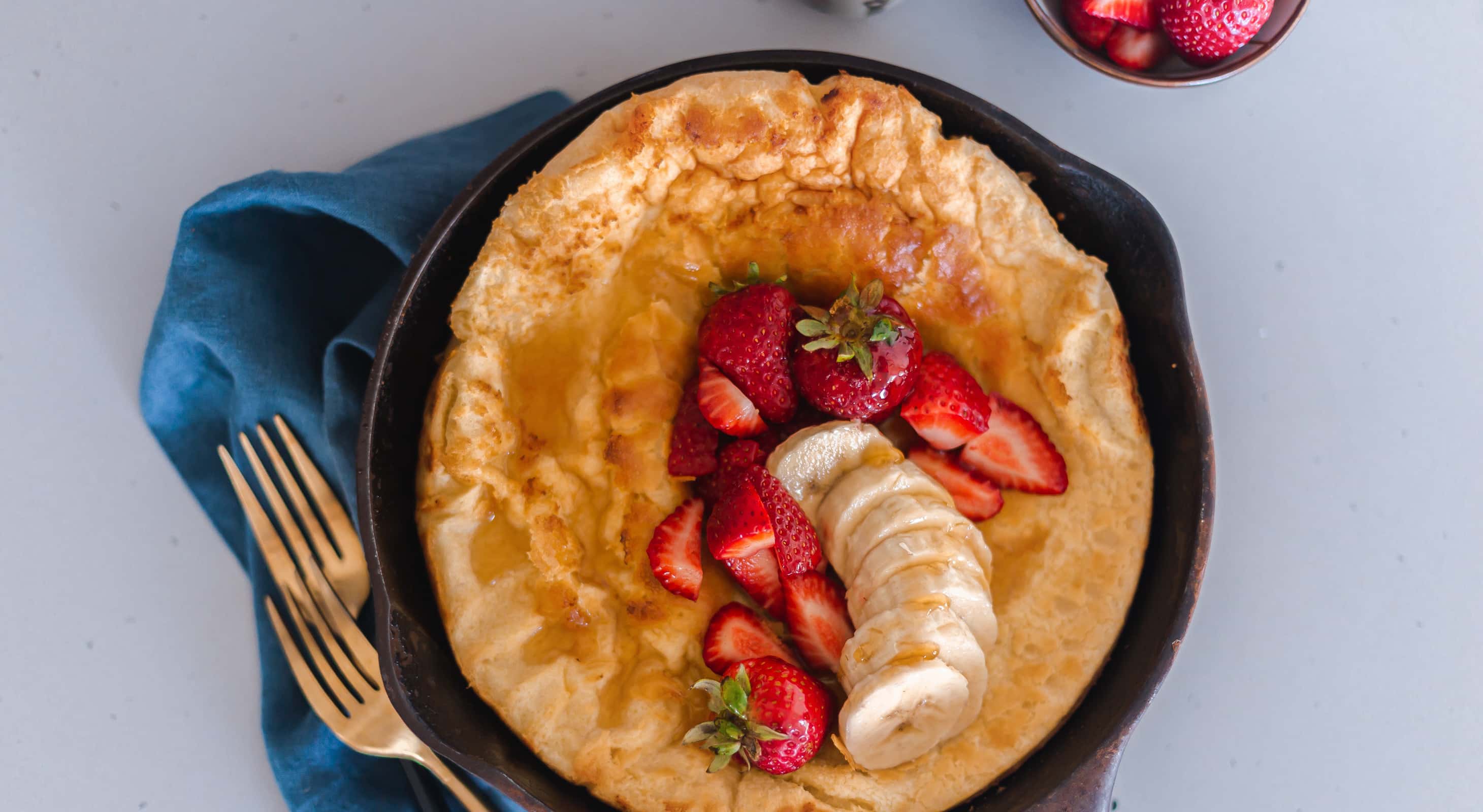 Puffed pancake in a cast iron skillet served with berries and banana