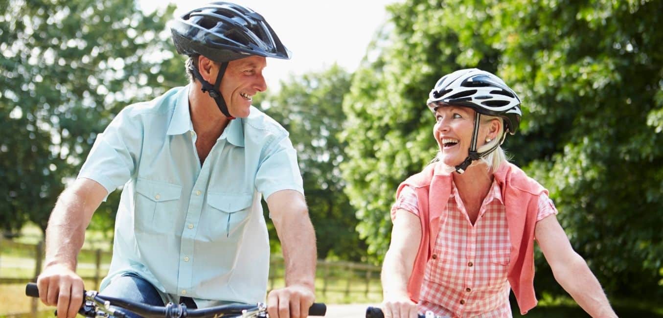 middle-aged couple looking at each other and smiling while riding bikes in the countryside