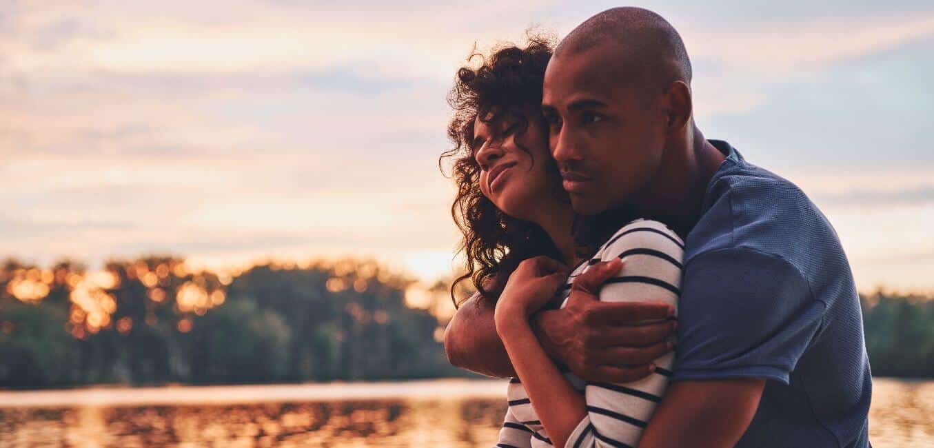 happy young couple embraces while overlooking river at dusk