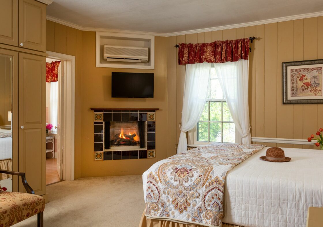 Paneled guest room with warm tones, carpeting and hardwood, corner fireplace, and storage.