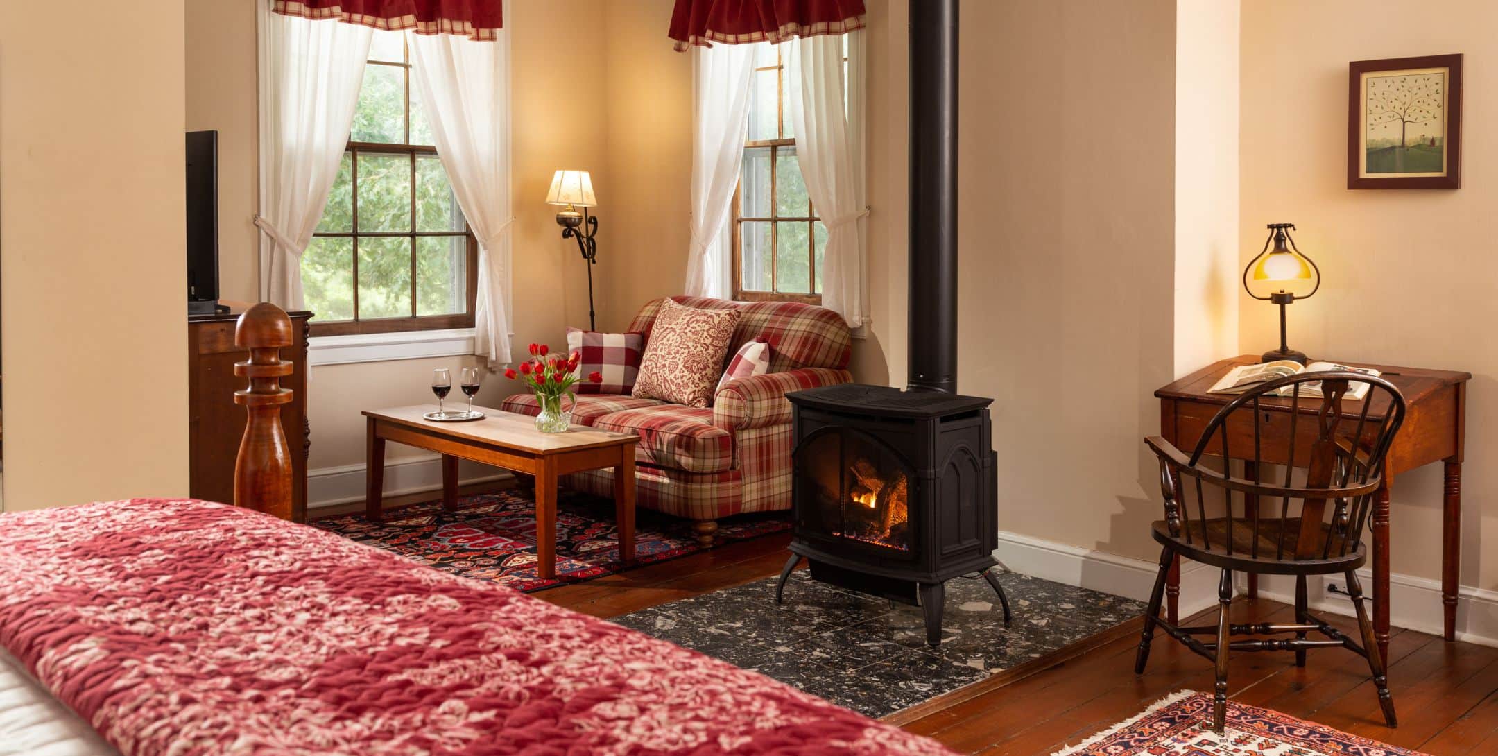 Red room with beige walls, red plaid love seat in sitting area with TV and fire stove, hardwood floors