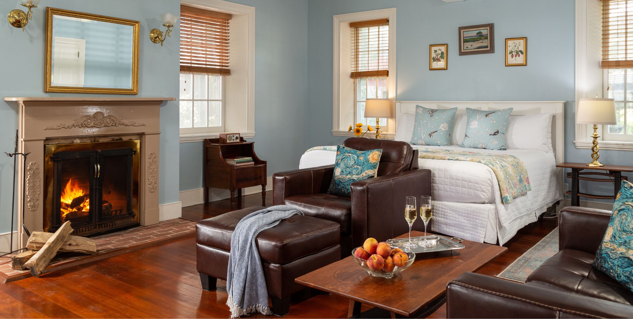 Light blue Sunrise Room with off-white king bed, natural light, fireplace with leather sitting area.
