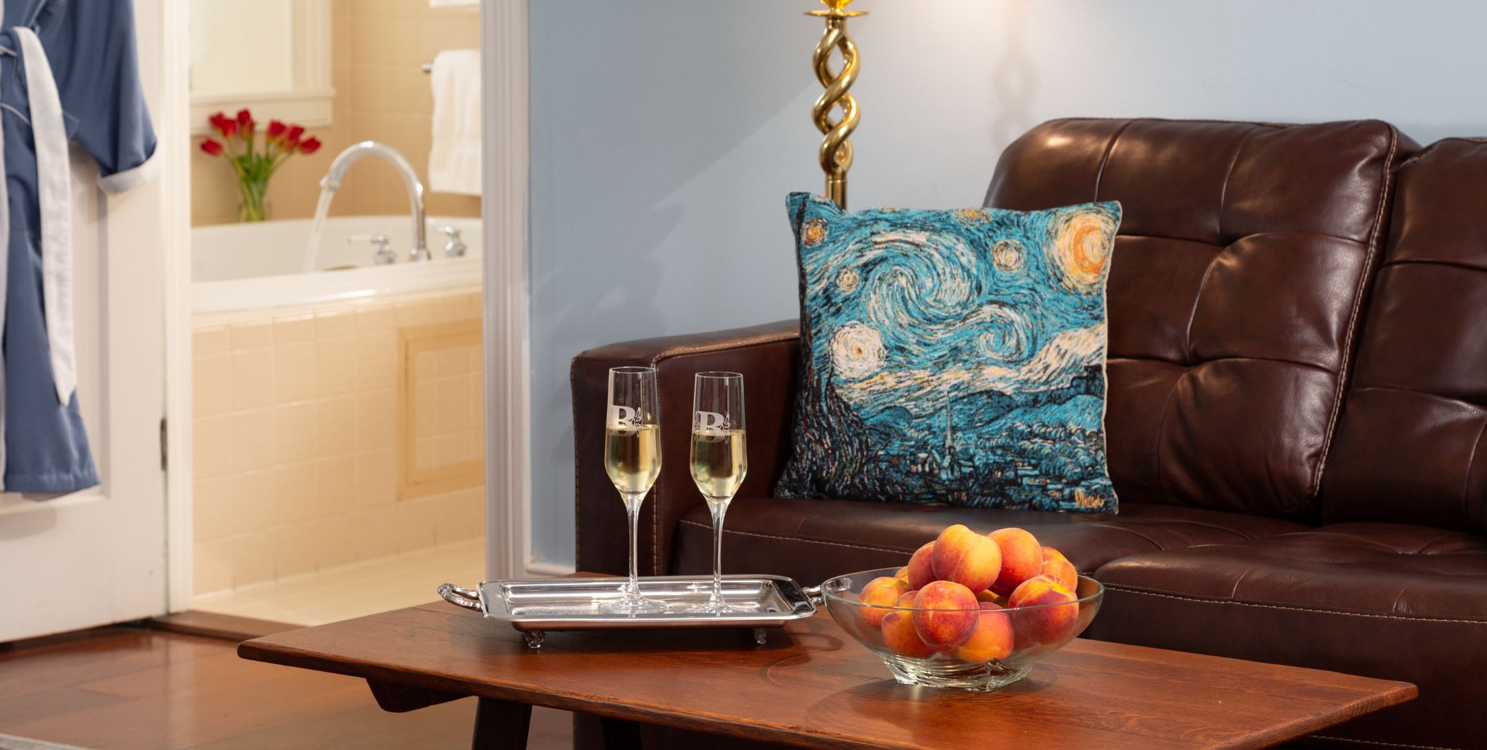 Leather loveseat and coffee table with fresh peaches and two Champagne flutes and a glimpse of the guest bath with fresh flowers