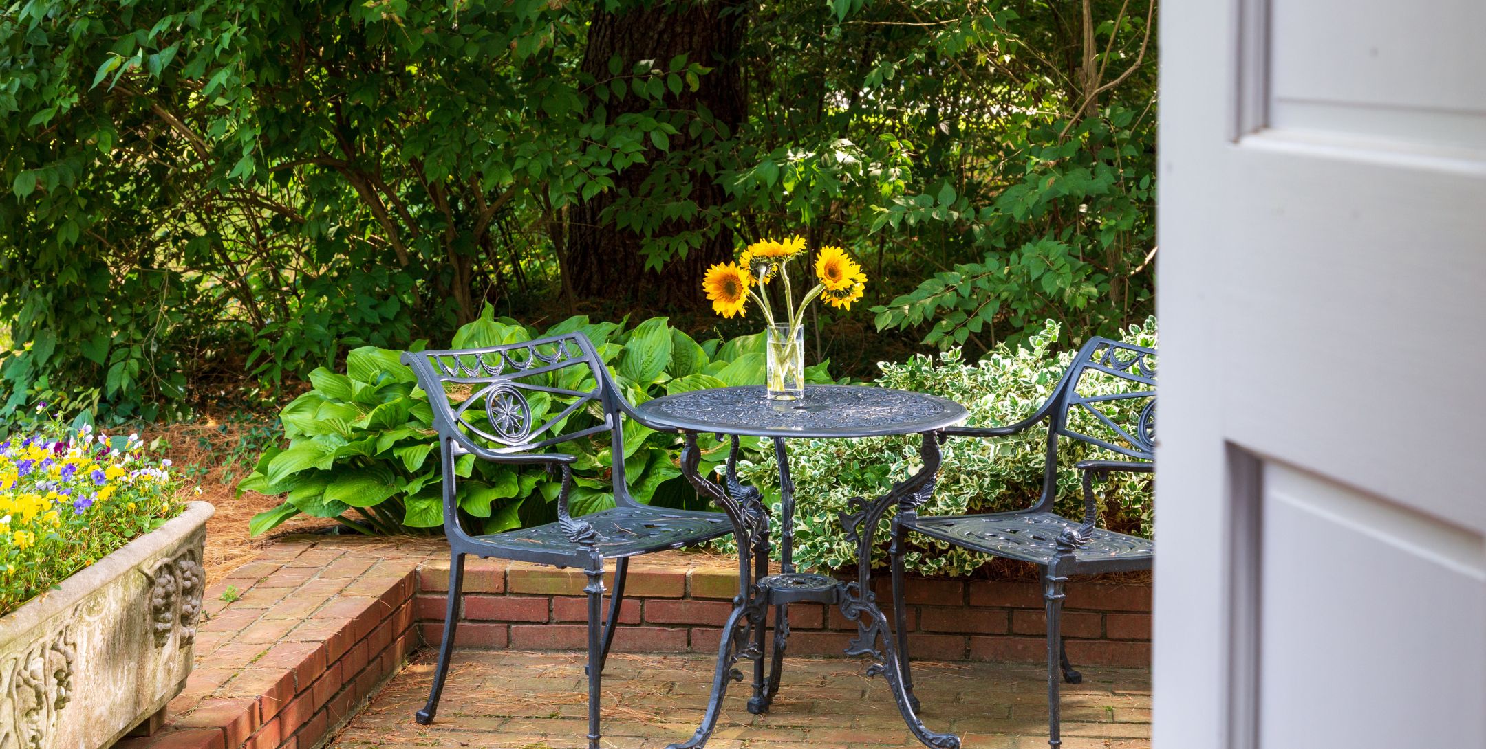 Brick patio with black metal patio table and chairs, and bright yellow sunflowers in a vase on the table