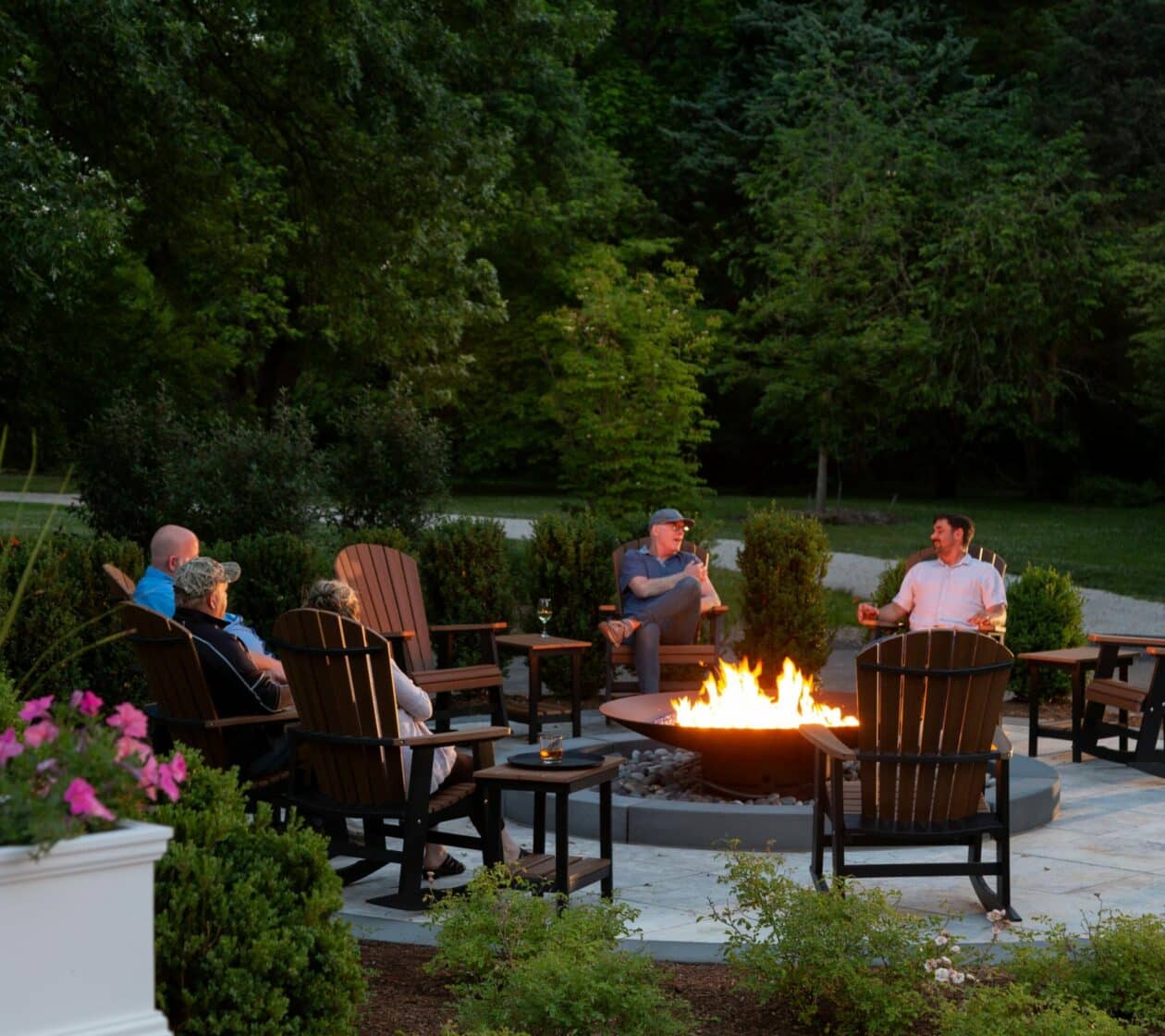 A group of friends gather around a fire pit and roast hotdogs