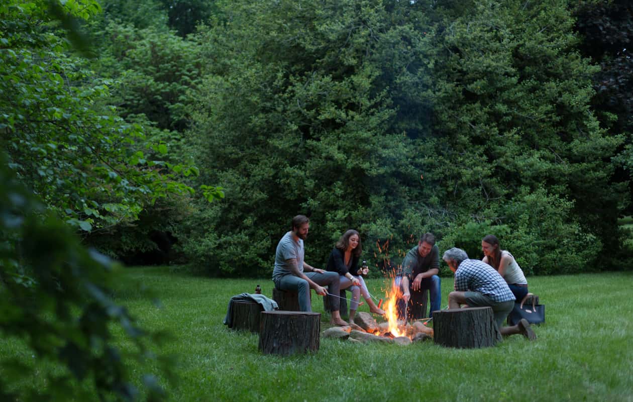 A group of friends gather around a fire pit and roast hotdogs