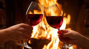 Toasting glasses of red wine in front of fireplace