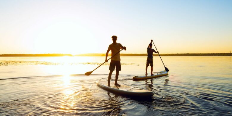 Two guys on paddleboards paddling around at sunset