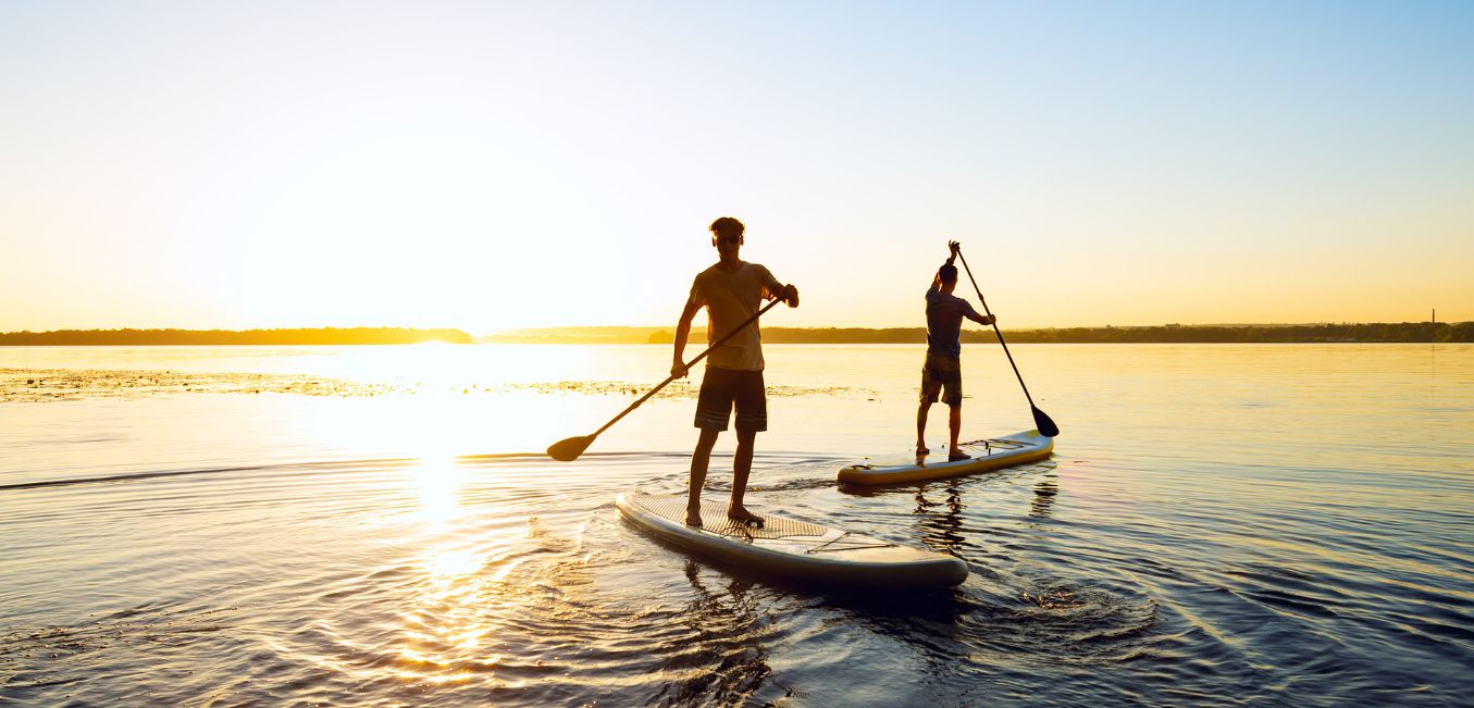 Two guys on paddleboards paddling around at sunset