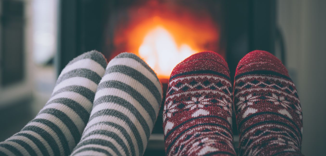A couple's feet in warm socks snuggled up close to a roaring fire in a fireplace