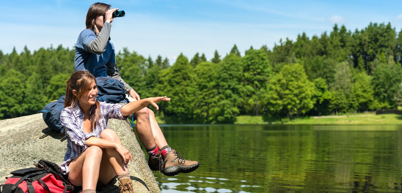 A couple sits on a rock at the edge of a lake while birdwatching