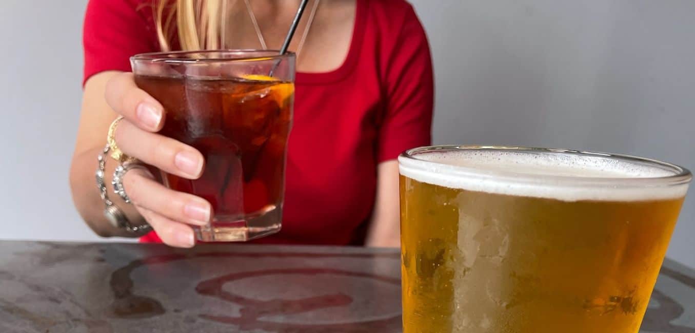 woman toasting with her drink and a glass of beer in the foreground