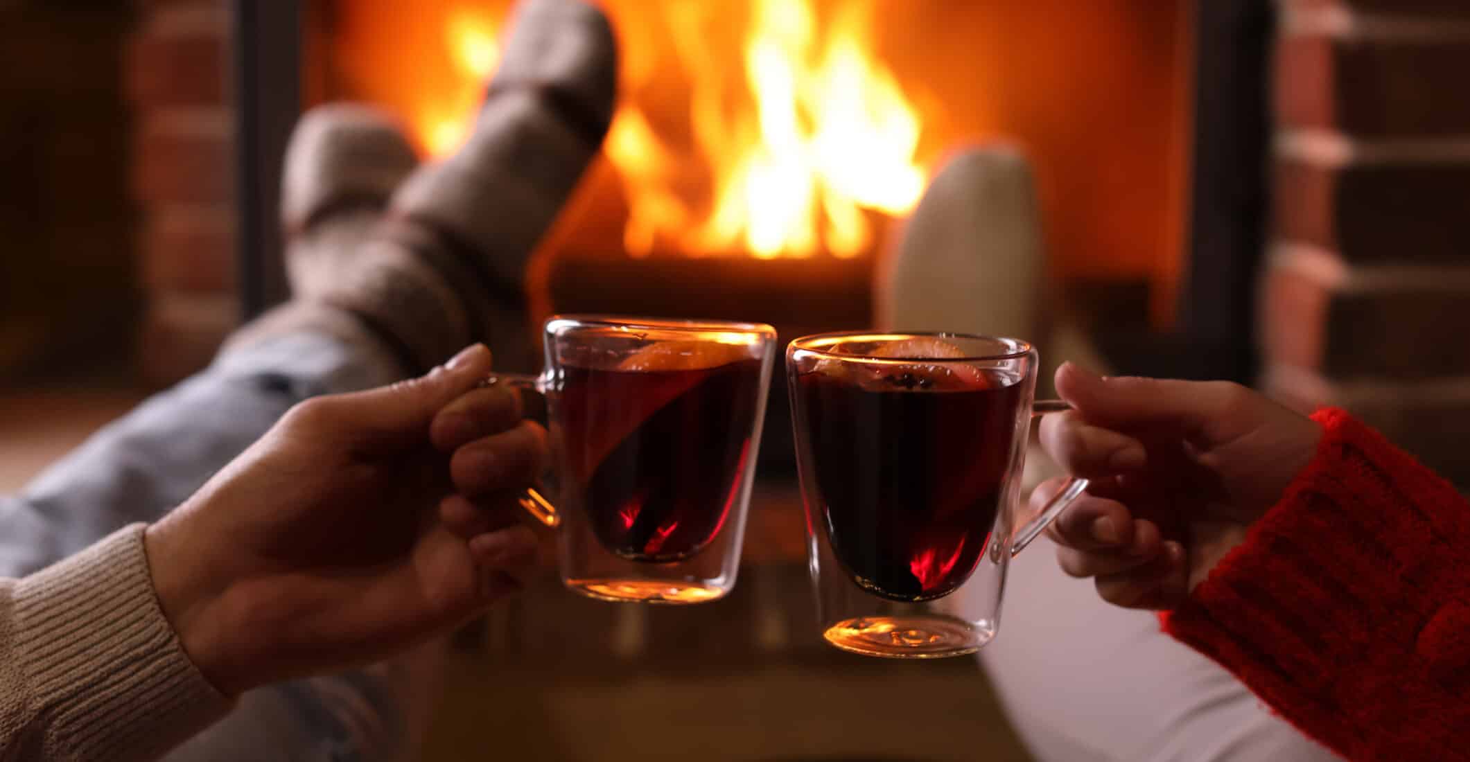 Couple with mulled wine near fireplace indoors, closeup. Winter vacation