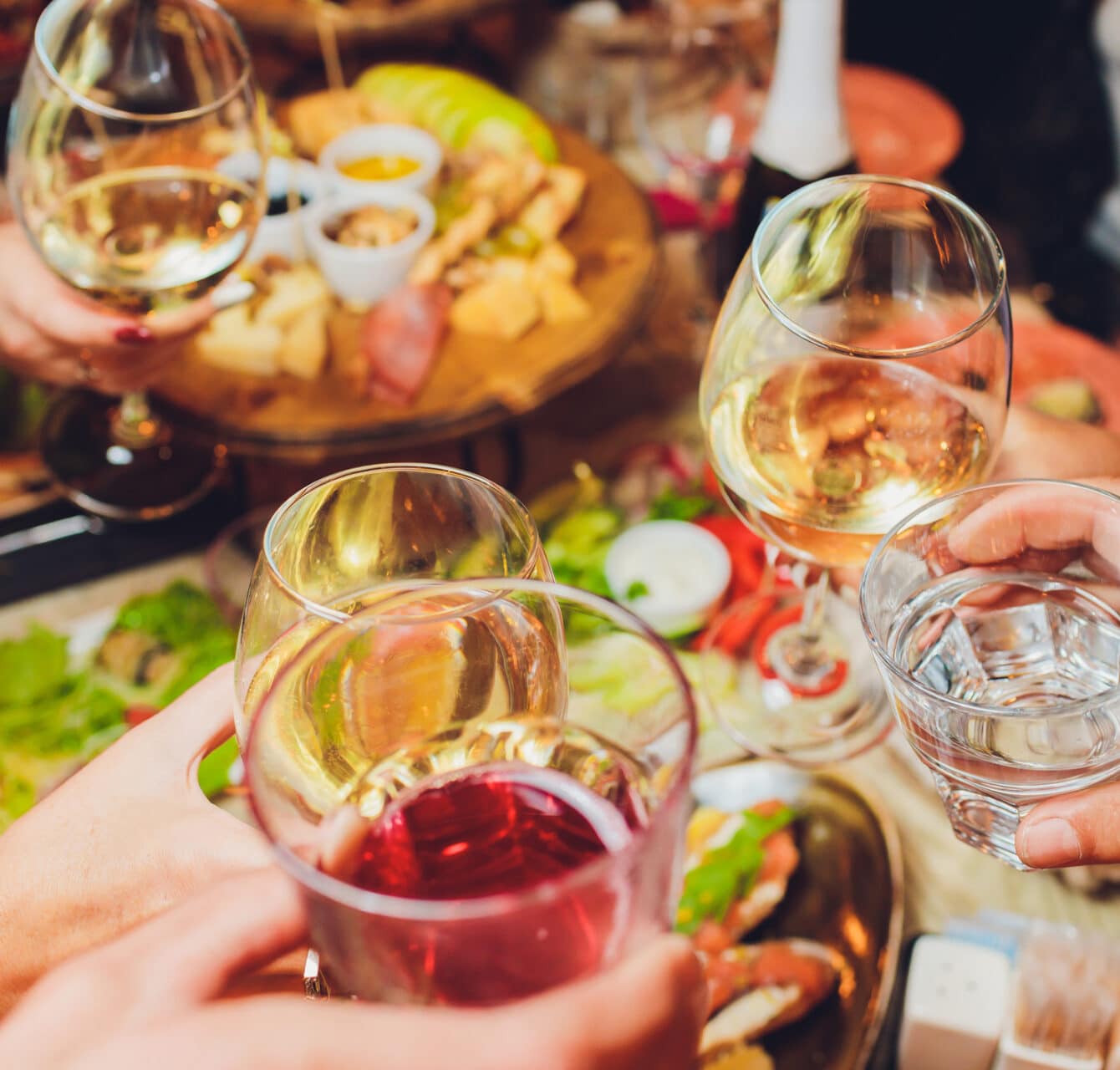 Friends clinking wine glasses over table of food.