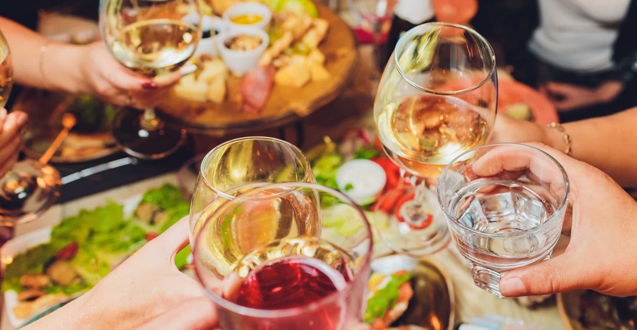 Friends clinking wine glasses over table of food.