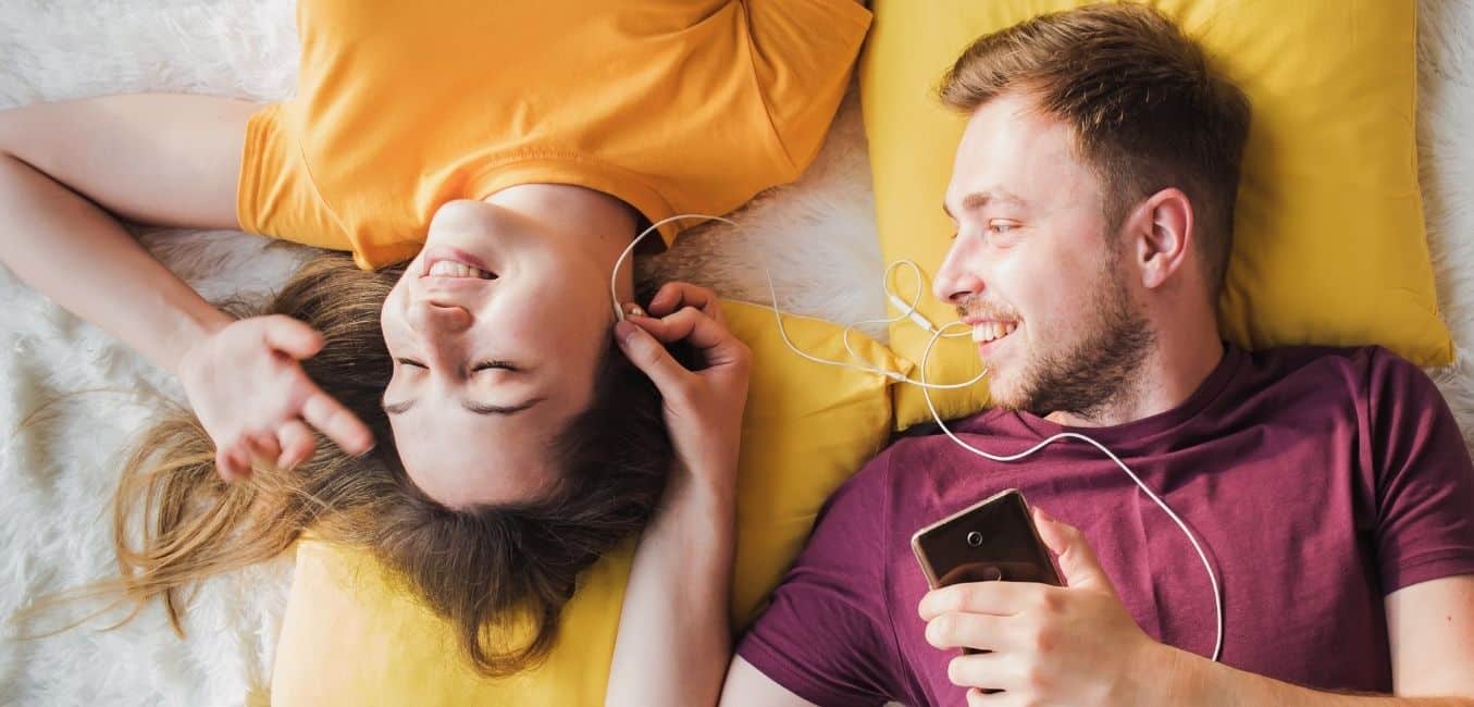 top view of couple lying down and sharing headphones with favorite playlist