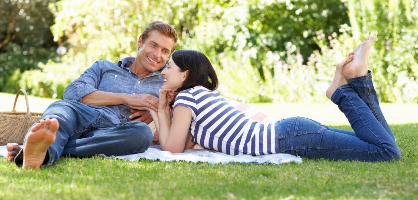 a couple relaxing on the grass with a picnic basket next to them