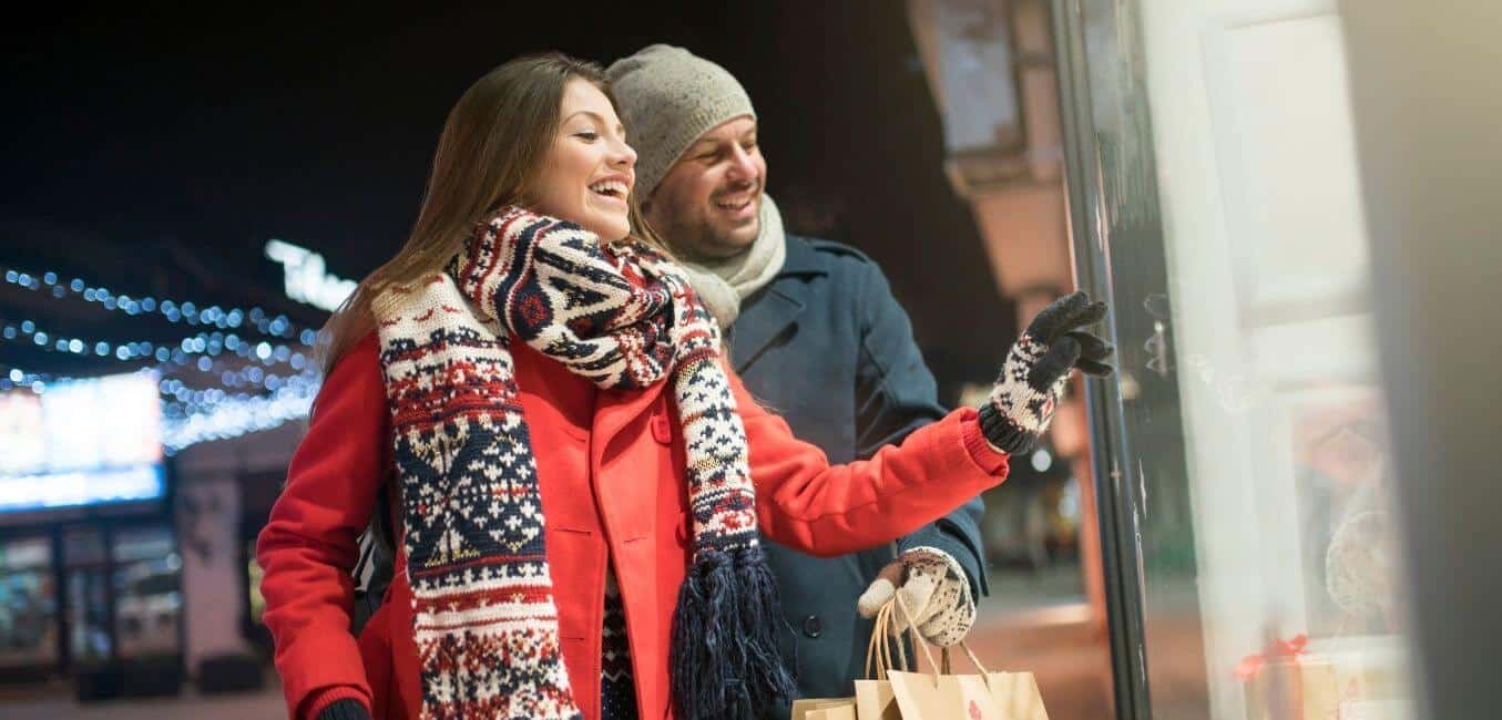 couple dressed in coats and hat smiling while looking in a shop window