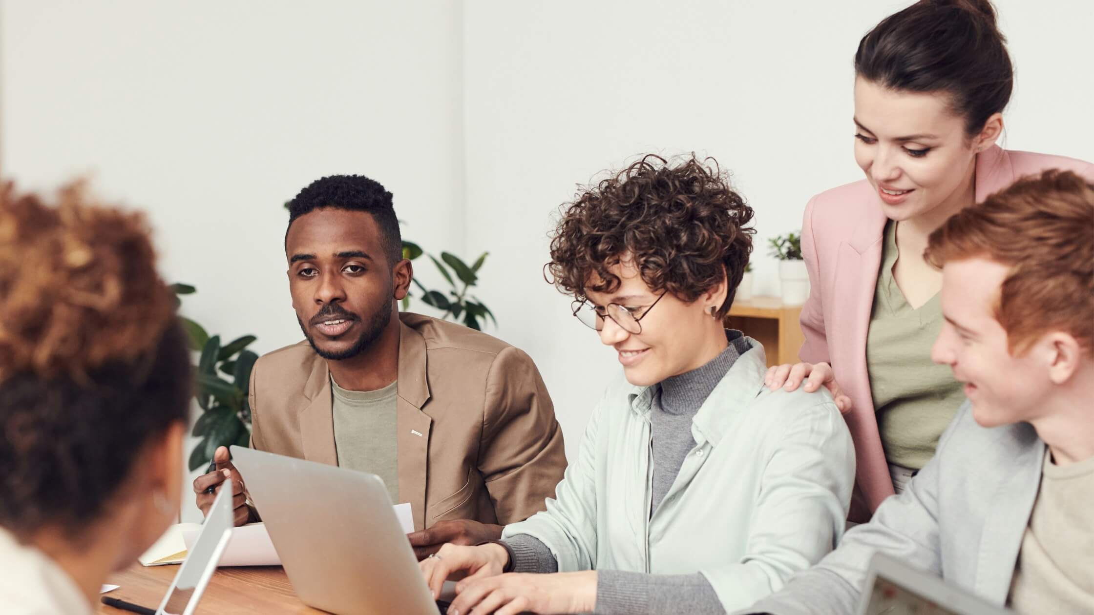 group of smiling individuals sitting around a conference table with open laptops