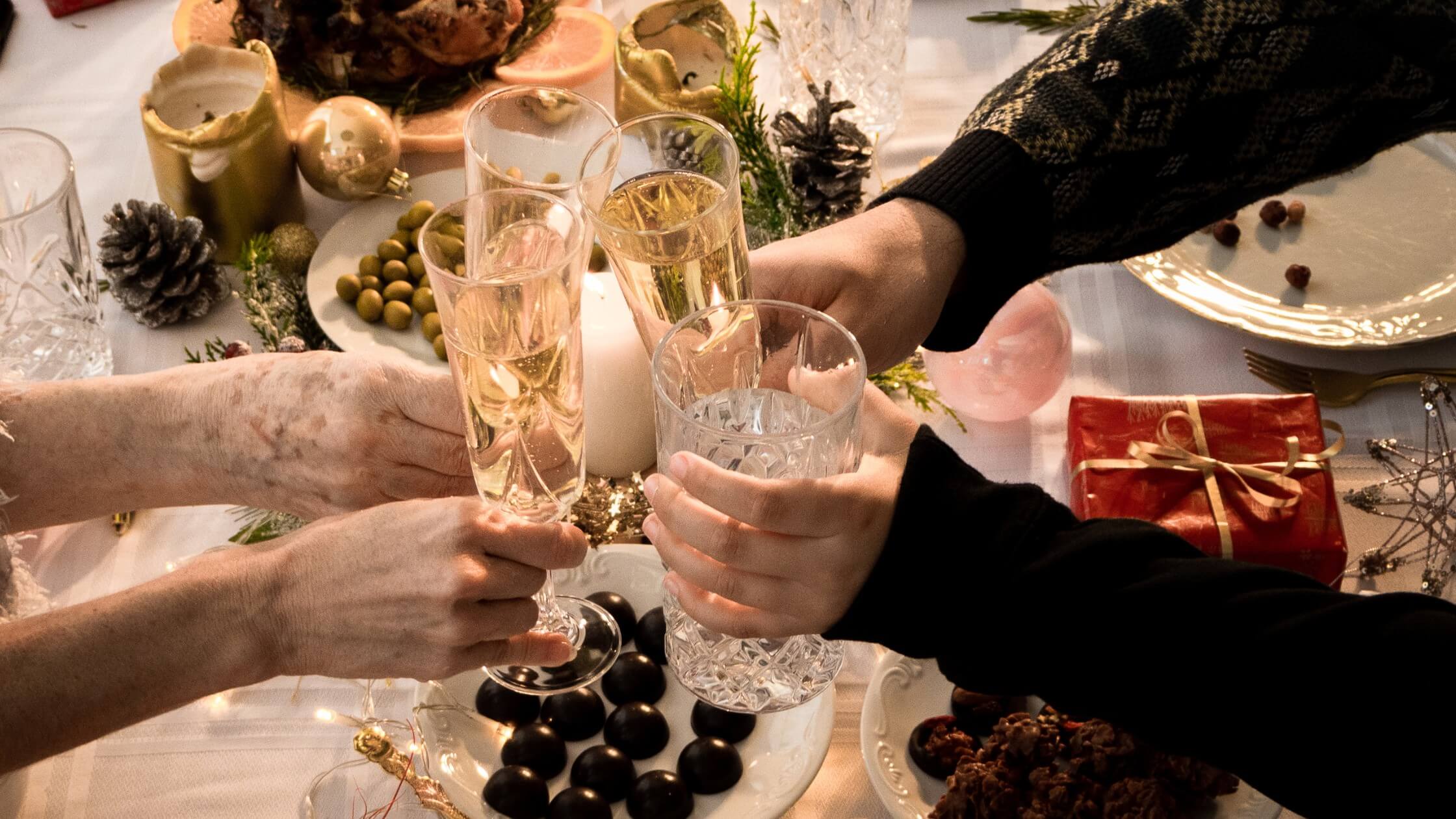 close up view of arms and hands hold various styles of glasses with beverages over dinner table