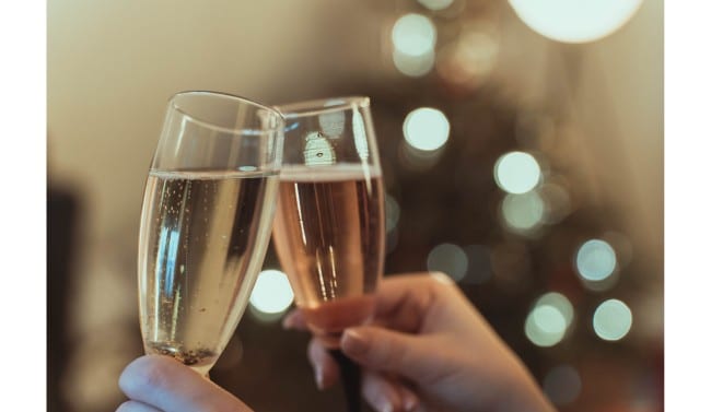 2 hands hold champagne glasses at an angle and clinking